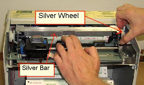 7. After the money order is hooked evenly on both of the black plastic tabs, slowly turn the silver wheel upward on the right side of the printer assembly.
