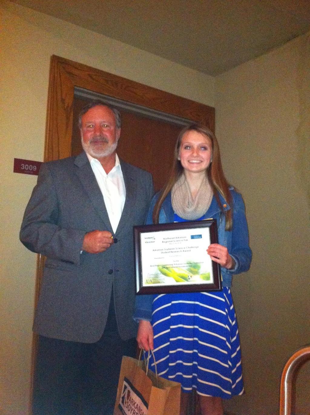 Rachel Milnes, holding her Arkansas Soybean Science Challenge Certificate and her tote bag of soybean-related items with Drew Oliver, Arkansas Soybean
