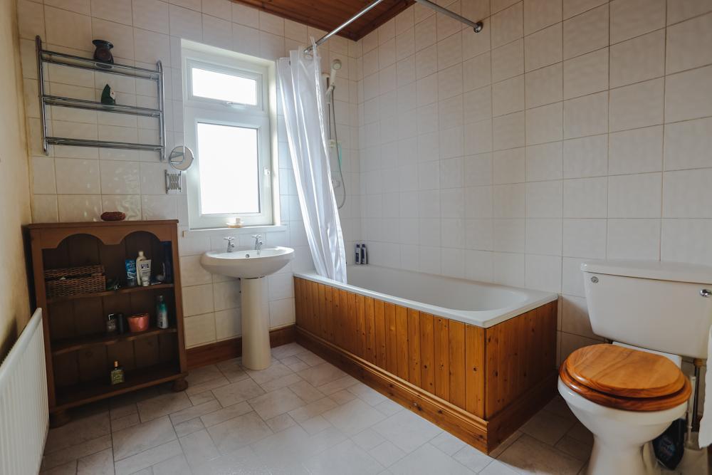Good Bathroom: 8/3 x 7/6 with fully tiled walls and ceramic tiled floor, pine tongue and groove sheeted ceiling, white suite comprising panelled bath with chrome twist grip taps, pedestal wash hand