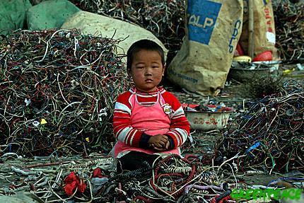 A Chinese child sits amongst a pile of wires and e-waste. Children can often be found dismantling e.