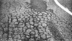 Compact Asphalt Concrete. Where the existing surface is badly cracked and loose (regardless of amount of distortion), remove old surface, tack area, and repair using Asphalt Concrete.