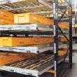 Pallets are loaded in sequence onto wheeled carriers of differing heights and are pushed back along inclined steel guide channels to