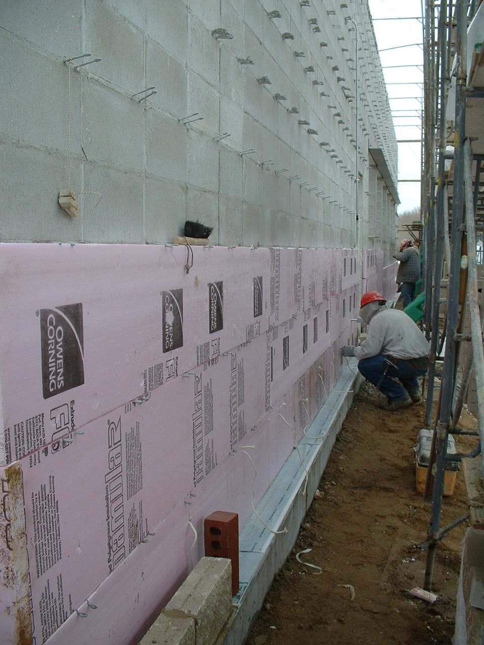 Photo 1 shows a cavity wall under construction inside a heated scaffold enclosure. The steel-reinforced concrete foundation is visible at the bottom of the wall.