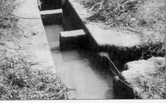 26 FIGURE 26 Long-crested weir in a small canal For smaller canals, other forms of weirs may be used, such as the type illustrated in Figure 26, where the weir is placed parallel to the long axis of