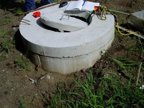 FIGURE 11-1: DUG WELL WITHOUT SEALED ACCESS AND IMPROPER MOUNDING Figure 11-1 shows an open access lid on a dug well cover. The open lid is allowing slugs to enter the well (see Figure 11-2).