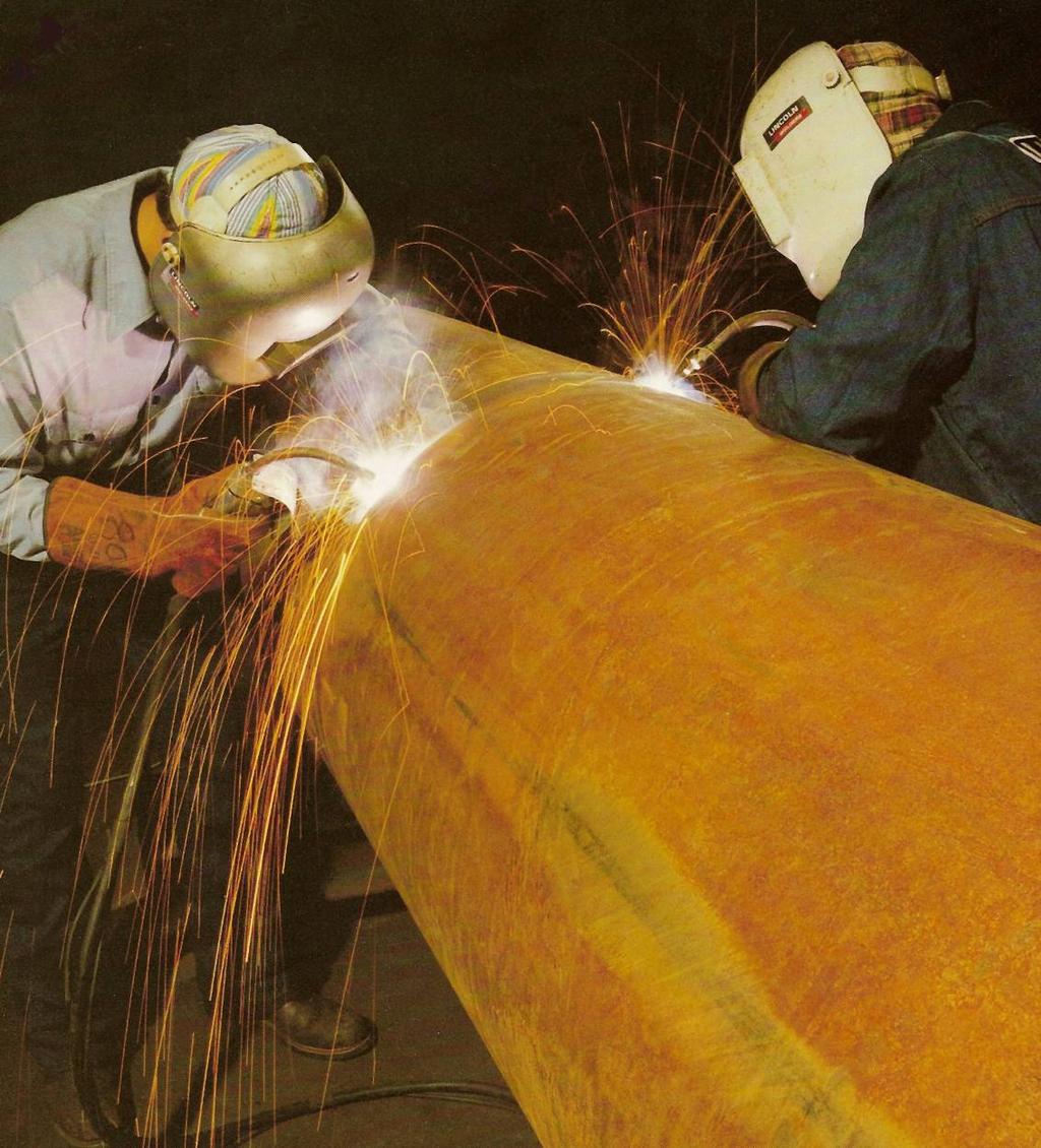 Two welders perform arc welding on a large steel pipe section