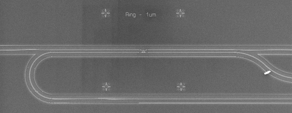 b) SEM image showing top view of a system of photonic waveguides connecting into the device of interest in the middle. In fig.
