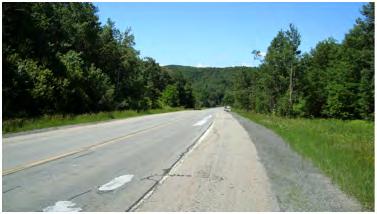 The vegetation on the north side of the road is set far back from the roads edge towards the center of the zone.
