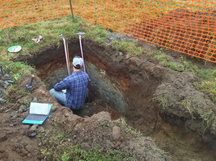 A student assessing soil horizons and layers in a soil test pit at