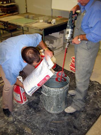 Pouring the Ardex FLC into the mixing container with the mixing water pre-batched using an Ardex water gauging bucket. The ribbon mixing paddle on the drill mixer can be clearly seen.