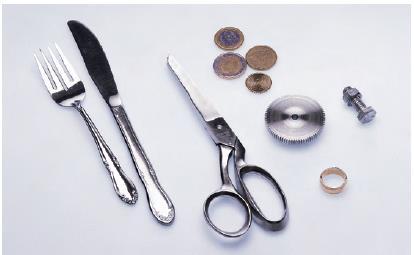 Familiar objects that are made of metals and metal alloys: (from left to right) silverware (fork and knife), scissors, coins, a gear, a wedding ring, and a nut and bolt.